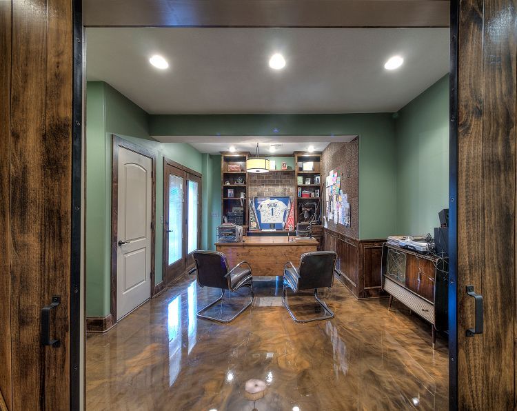 Home office with sage green walls, wooden desk, two chairs, and a polished metallic floor seen through wooden barn doors.