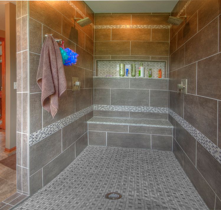 Walk-in shower with brown tiled walls, a built-in bench, a mosaic tiled niche, and a hanging towel.