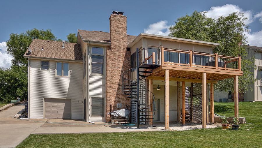 A two-story suburban house with a brick chimney, wooden deck, spiral staircase, and an attached garage.