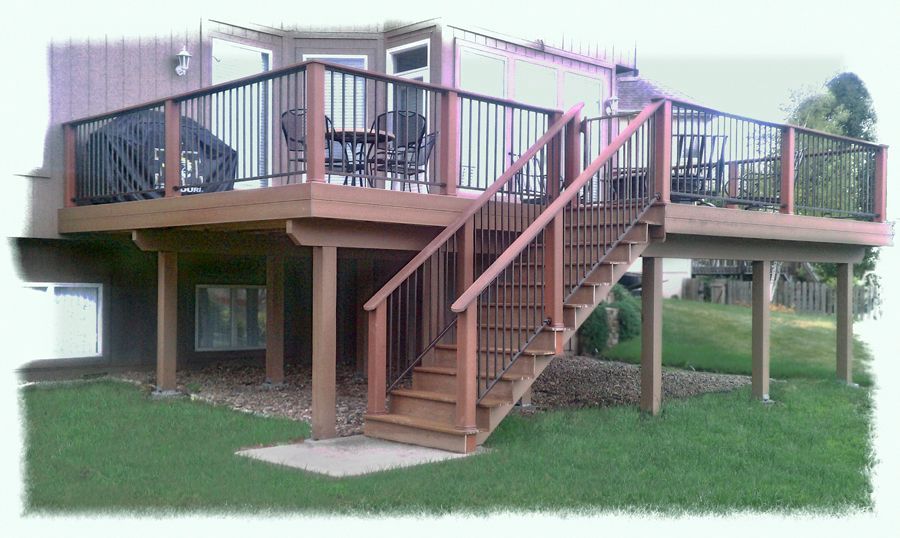 An elevated wooden deck with black metal railings and stairs leading down to a green lawn.