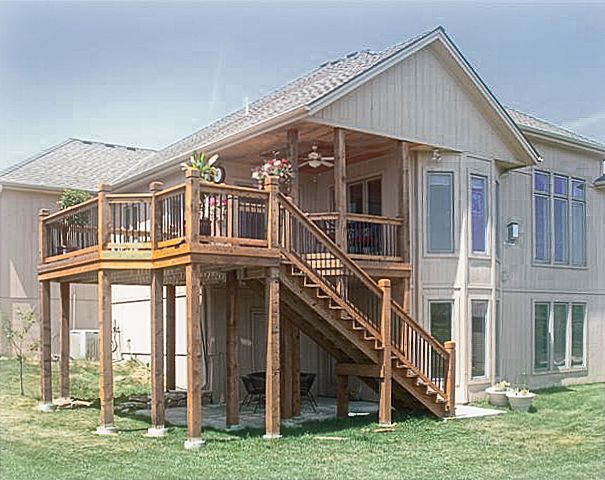 A raised wooden deck with a staircase attached to the back of a light-colored two-story suburban house.