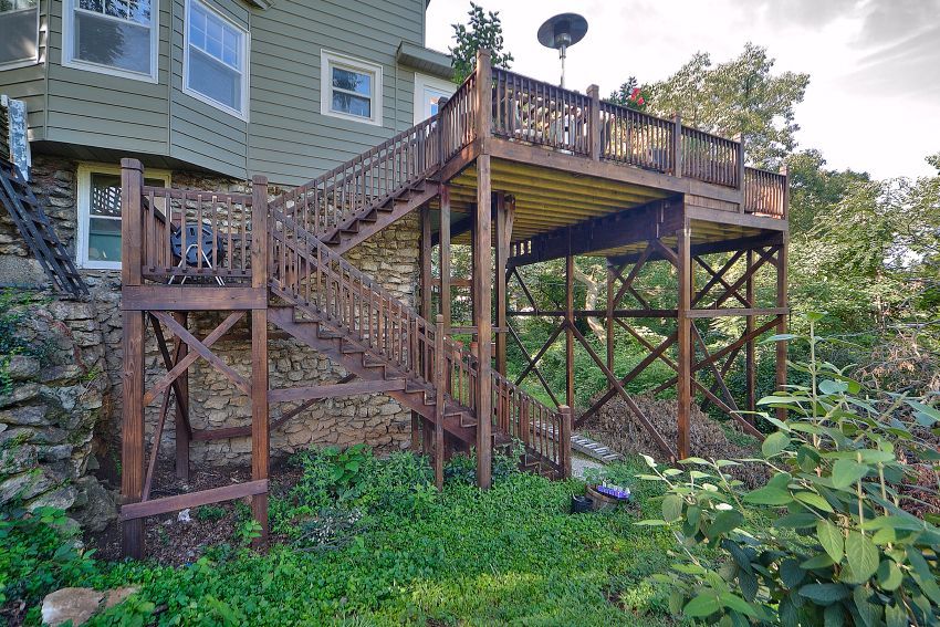 A large, elevated wooden deck attached to the back of a light green house, featuring a long staircase with a landing.
