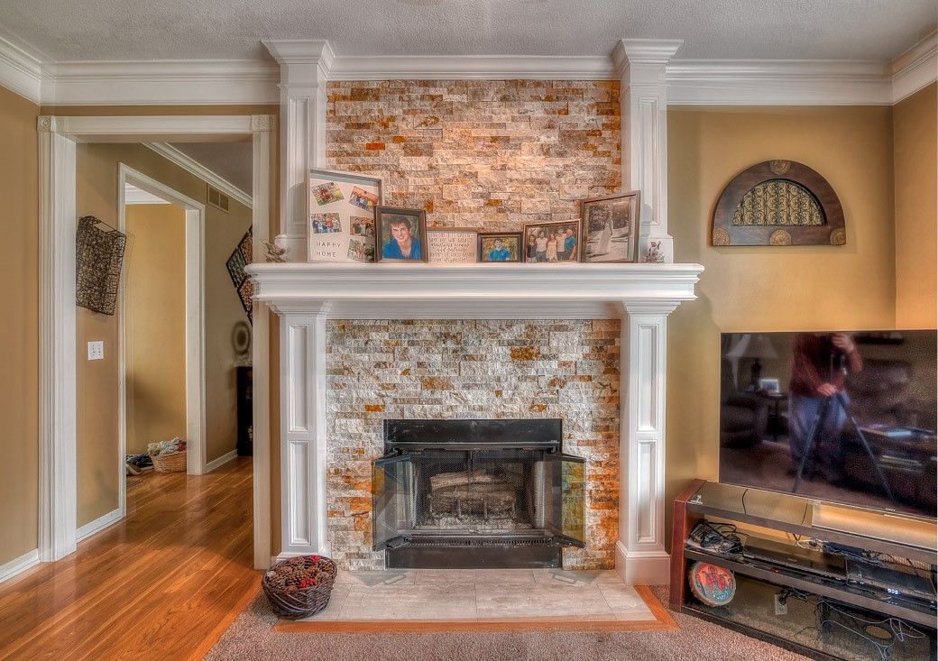 A stone fireplace with a white mantel and a TV on a stand to its right, set in a living room with hardwood floors.