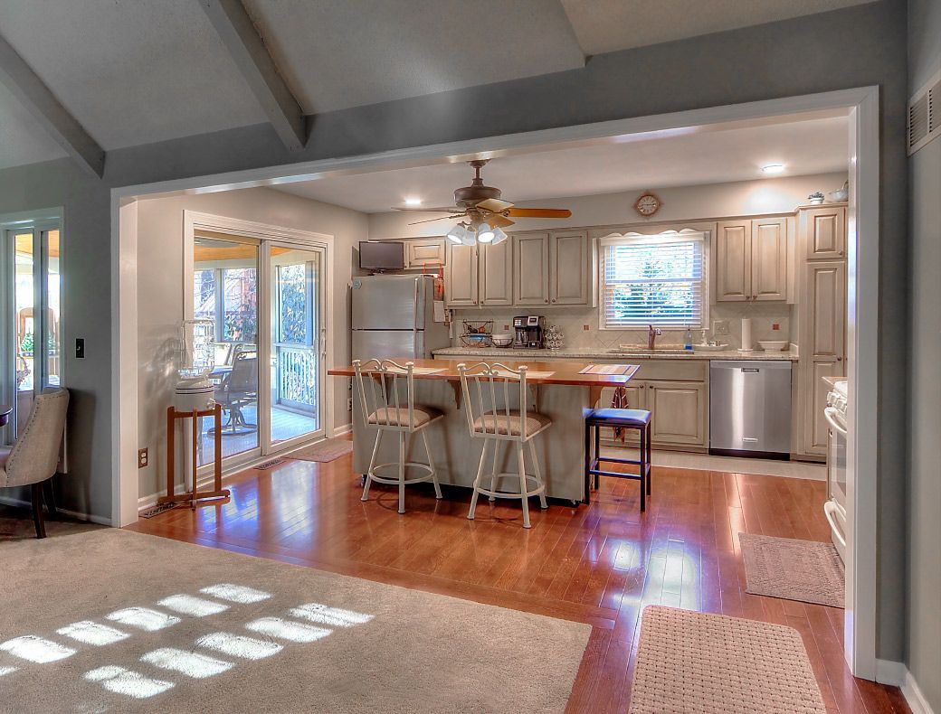 A kitchen with white cabinets, a wooden island with two stools, stainless steel appliances, and wood floors.