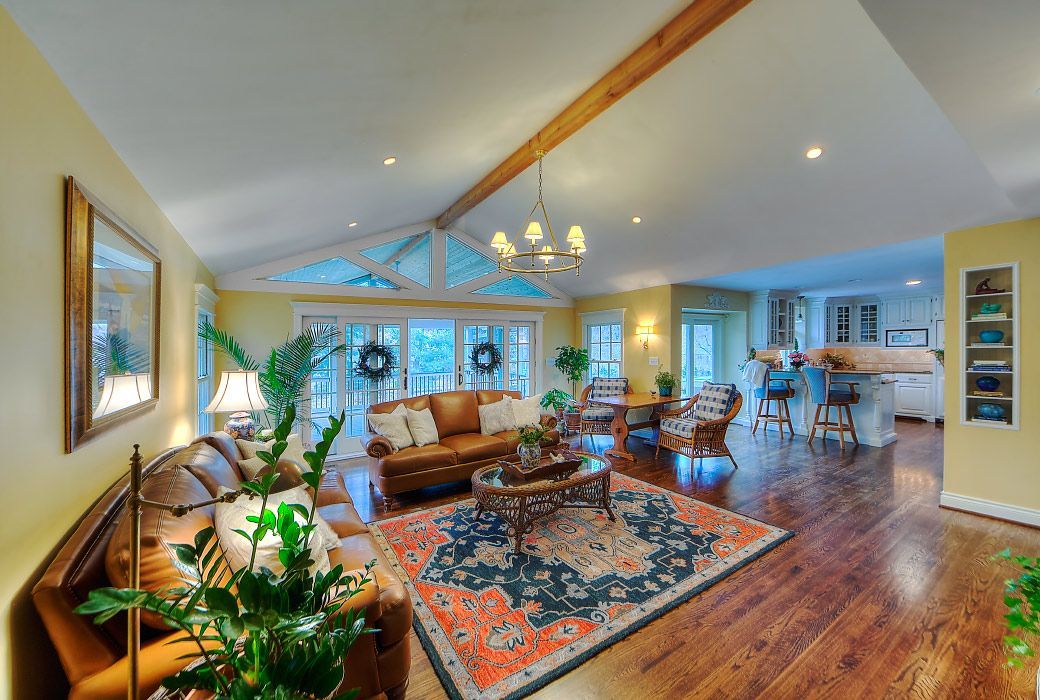 A spacious, sunlit living room with hardwood floors, a brown sofa, a patterned area rug, and an open-concept kitchen.