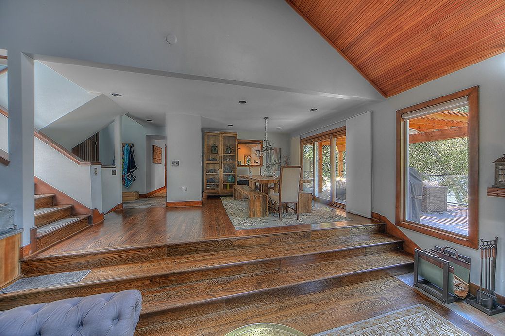 A split-level interior space with a raised dining area, wooden floors, stairs, and a large window under a vaulted ceiling.