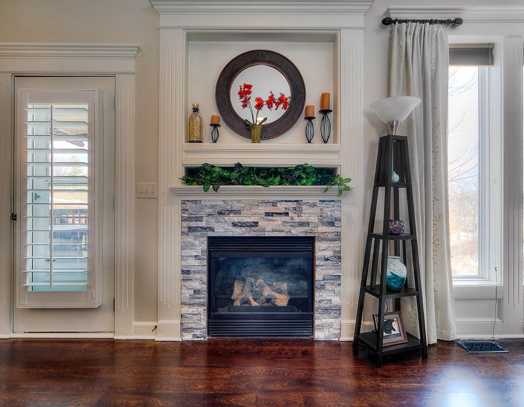 A fireplace with a stone surround, topped by a built-in shelf containing a decorative wreath and items in a living room.