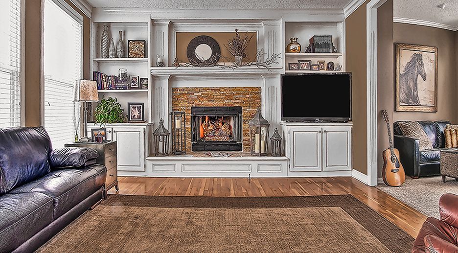 A living room features a white built-in fireplace and shelving unit, a dark leather sofa, and a large brown area rug.