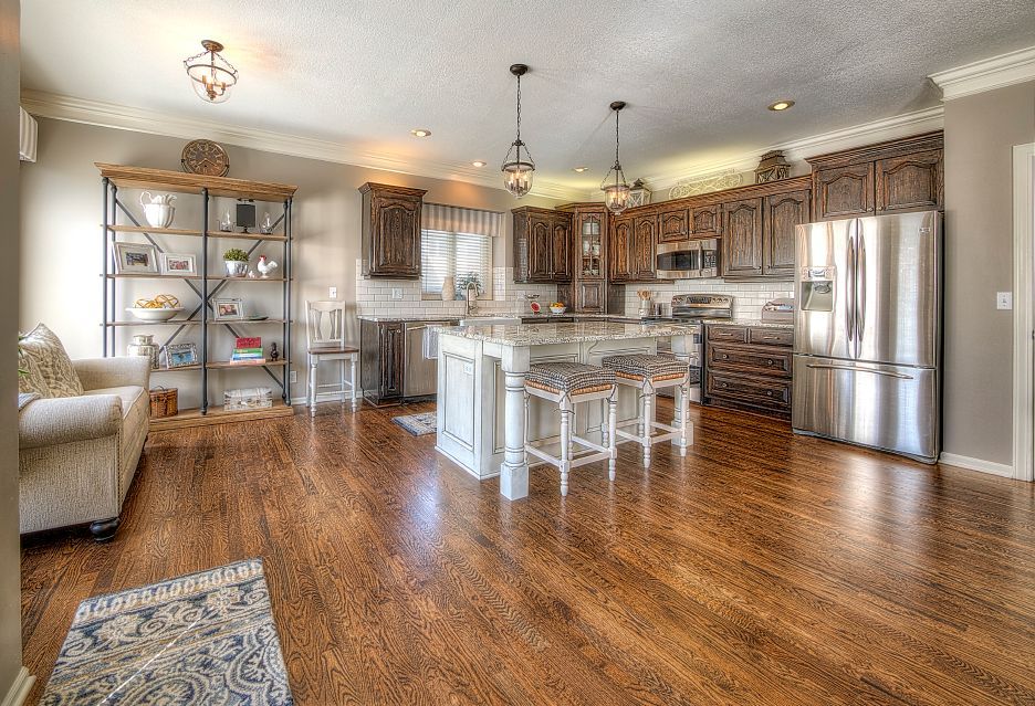 A kitchen with dark wood cabinets, a white island with stools, a stainless steel refrigerator, and wood flooring.