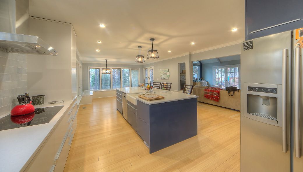 Modern open-plan kitchen with white cabinets, a large blue island, stainless steel refrigerator, and hardwood floors.