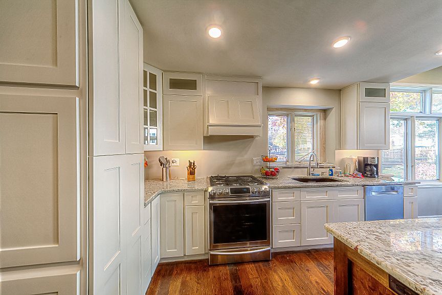 A modern kitchen with white cabinets, granite countertops, stainless steel appliances, and wood flooring.