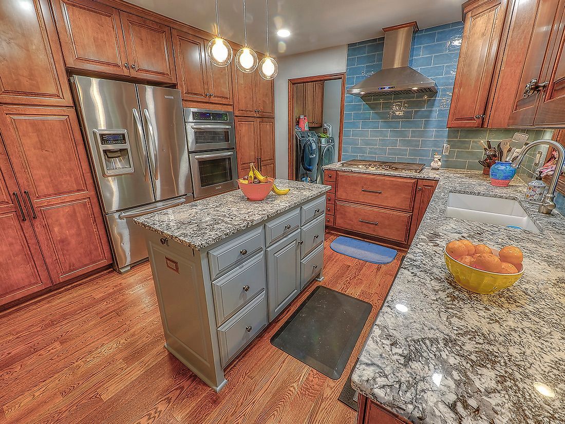 A kitchen with wood cabinets, a gray center island, granite countertops, and a stainless steel refrigerator and oven.