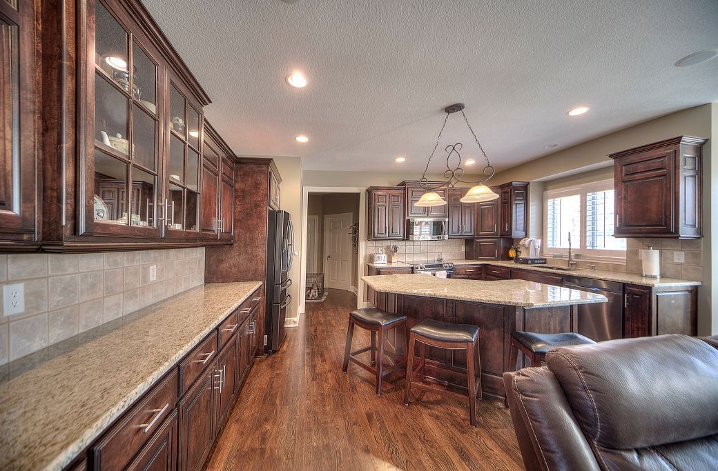 A kitchen with dark wood cabinets, granite countertops, a central island with bar stools, and wood flooring.