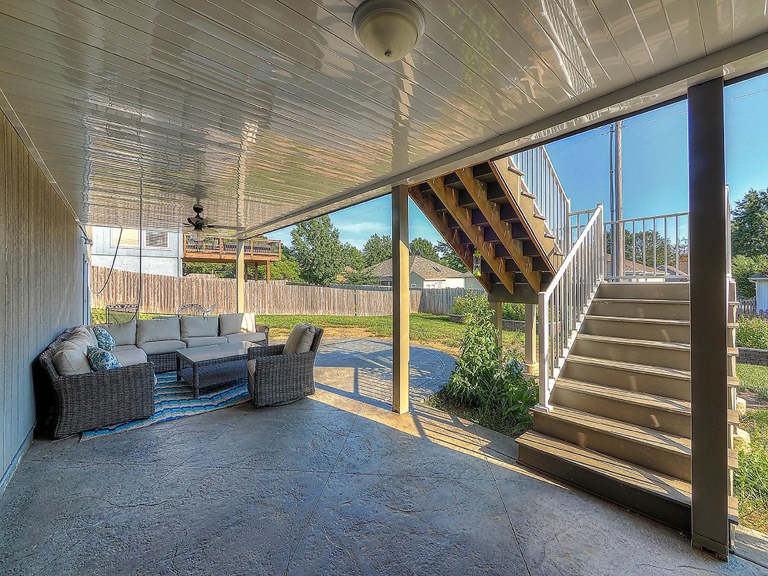 A covered patio with outdoor furniture and a set of wooden stairs leading up to an elevated deck.