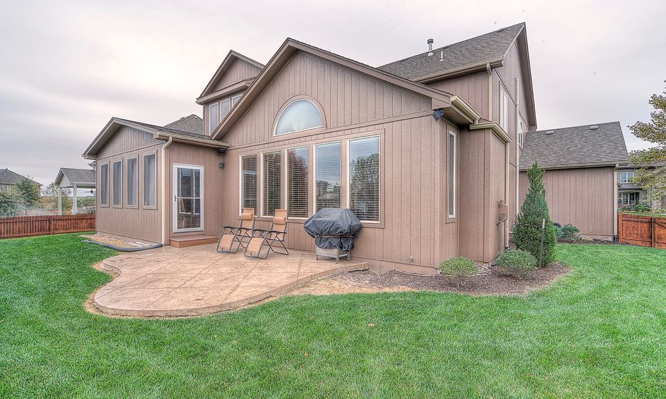 A brown, two-story house with a patio, lawn, and large windows on a cloudy day.