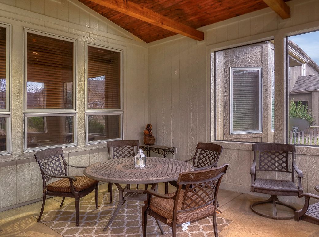 A sunroom with a round metal dining table, four chairs, and a brown patterned rug under a wood-paneled ceiling.