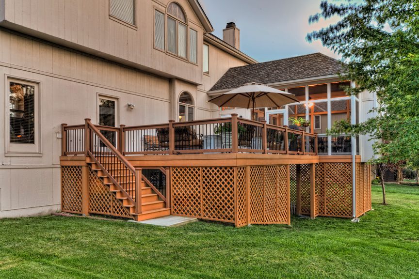 A multi-level wood deck with lattice skirting and a staircase, attached to the back of a light-colored two-story house.