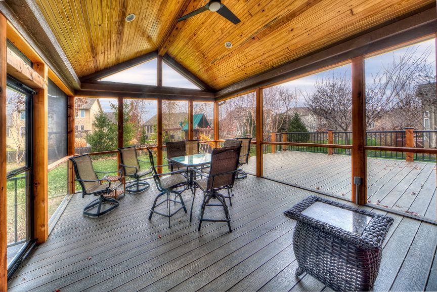 A screened-in wooden porch with patio furniture, including a table and chairs, overlooking a residential backyard.