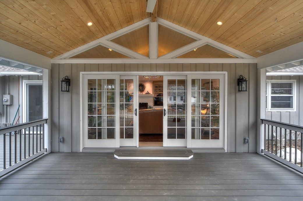 A covered wooden porch featuring a central set of French doors leading into a warmly lit interior space.