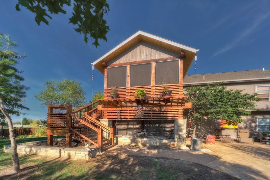 A raised wooden screened-in porch with a staircase, attached to a house under a clear blue sky.