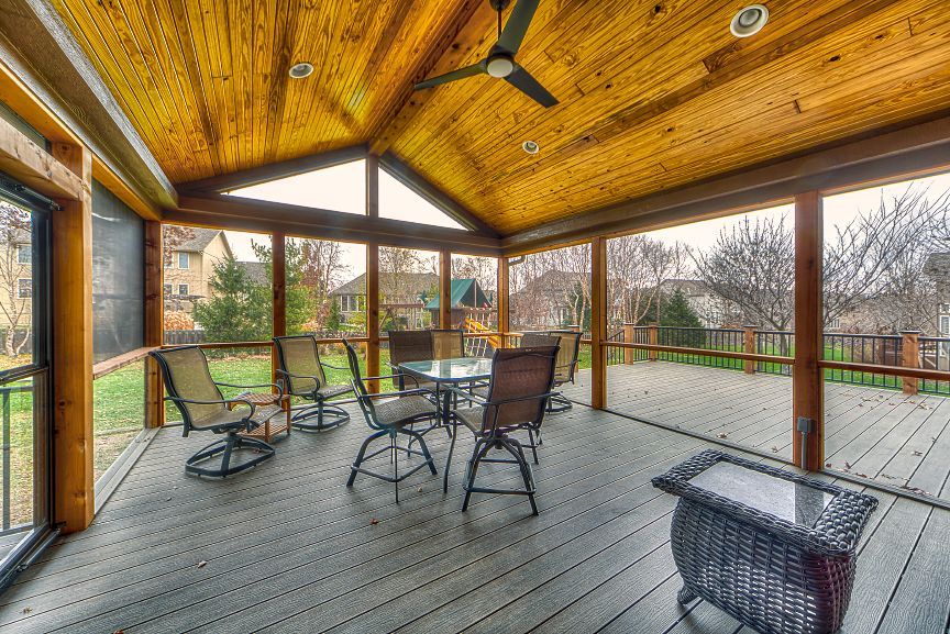 A screened-in wooden porch with a dining set and wicker furniture, overlooking a backyard at dusk.