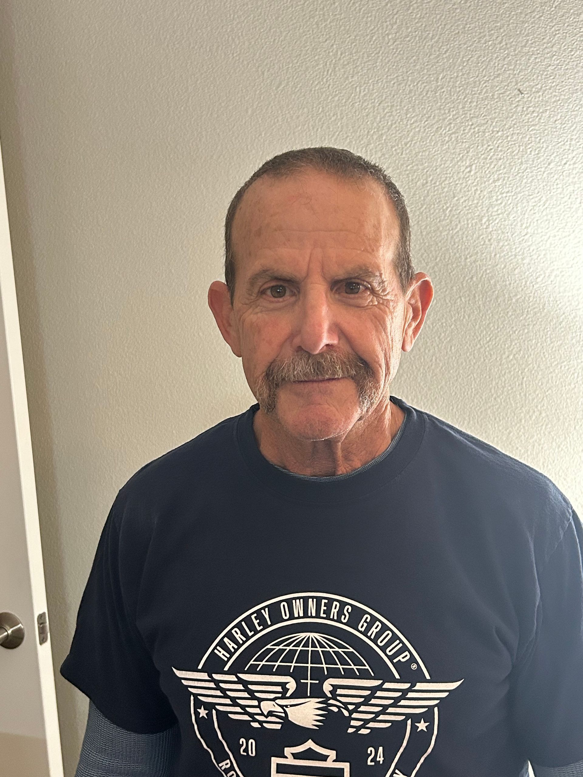 A man with a mustache is wearing a harley davidson t-shirt.