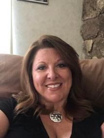 A woman is sitting on a couch wearing a black shirt and smiling.