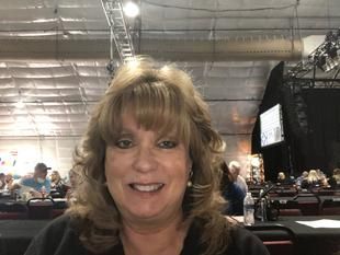A woman is smiling for the camera while sitting at a table in a room.