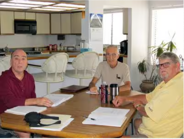 Three men are sitting around a table in a kitchen