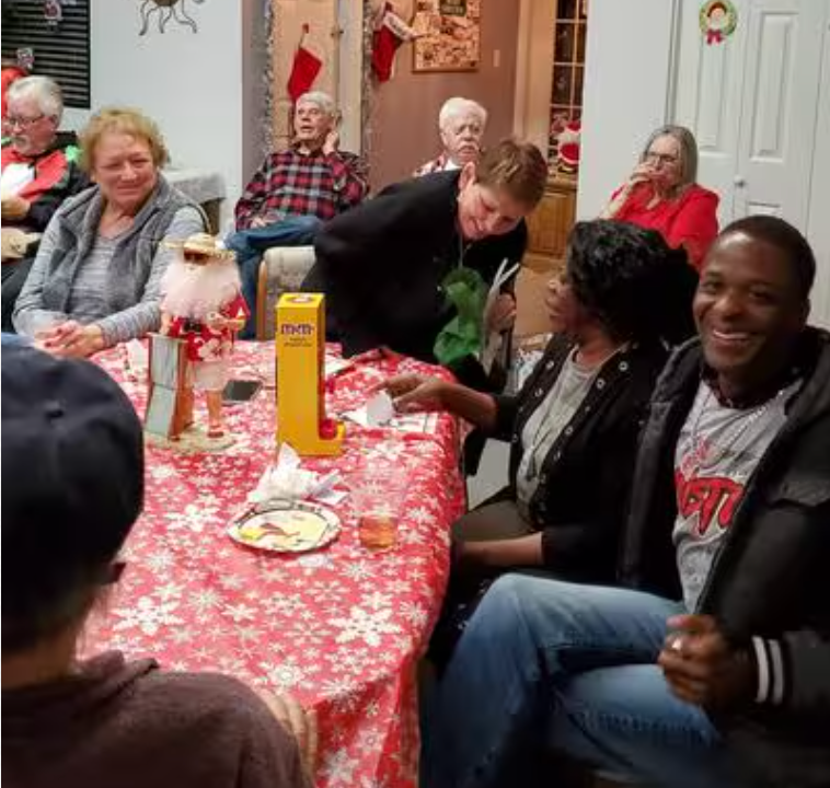 A group of people are sitting around a table with a red table cloth.