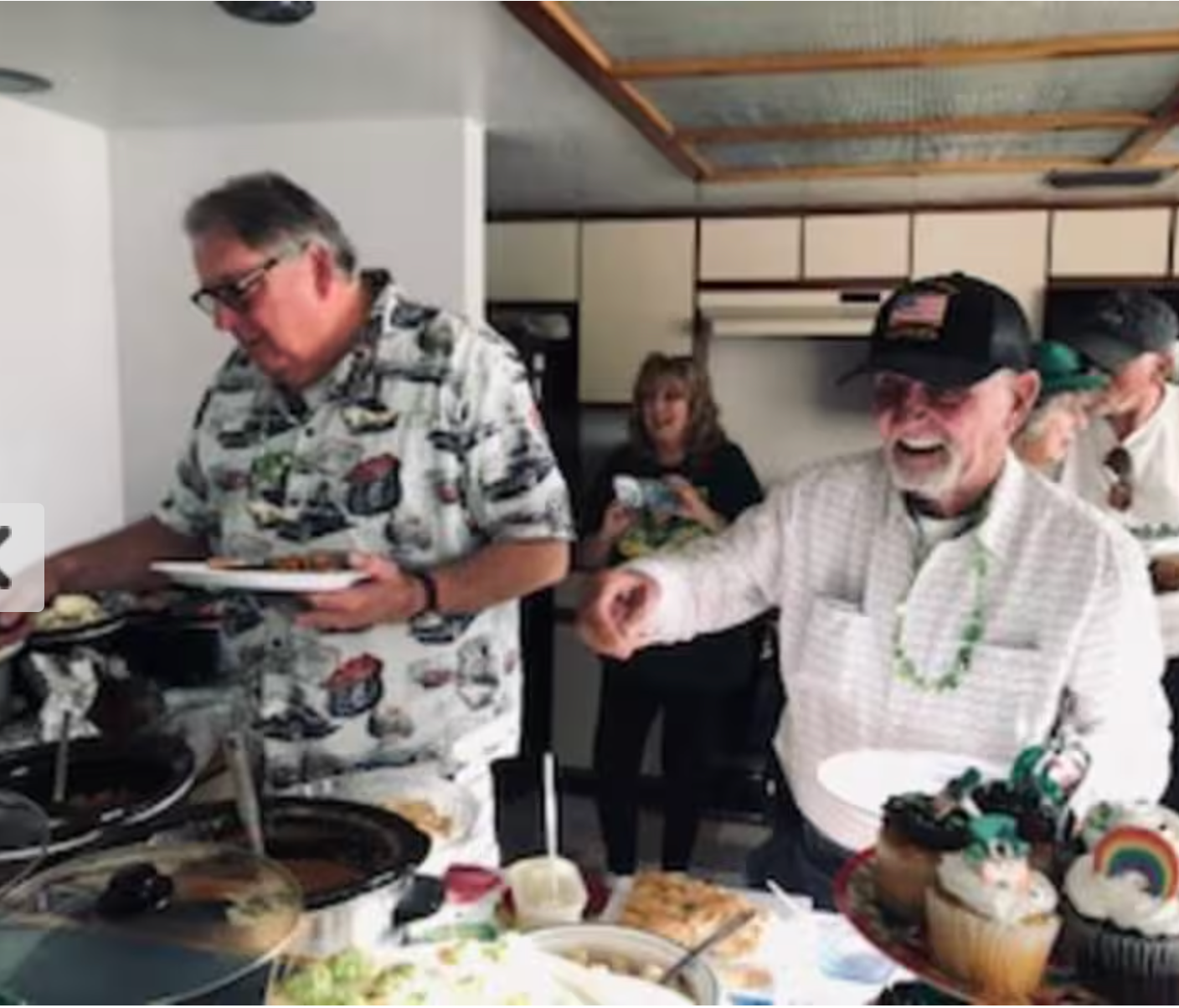 A group of men are standing around a table with plates of food.