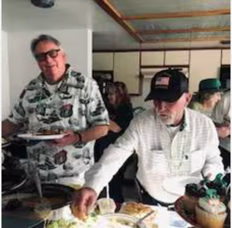 A group of men are standing around a table eating food.