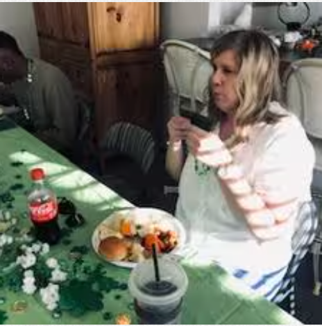 A woman is sitting at a table eating food and drinking soda.
