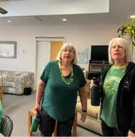 Two women are standing next to each other in a living room holding water bottles.