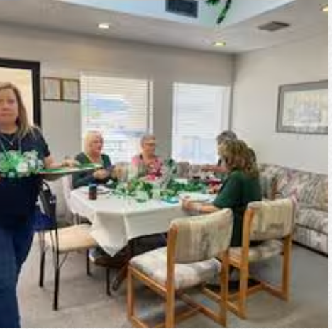 A woman is carrying a tray of food to a group of people sitting at a table.