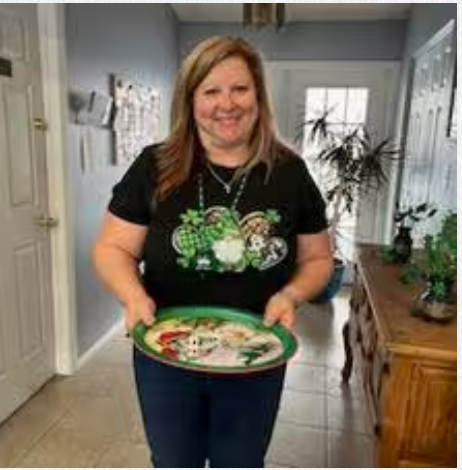 A woman in a black shirt is holding a green tray in a hallway.