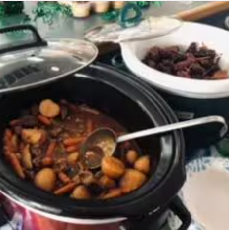 A crock pot filled with food and a spoon in it.