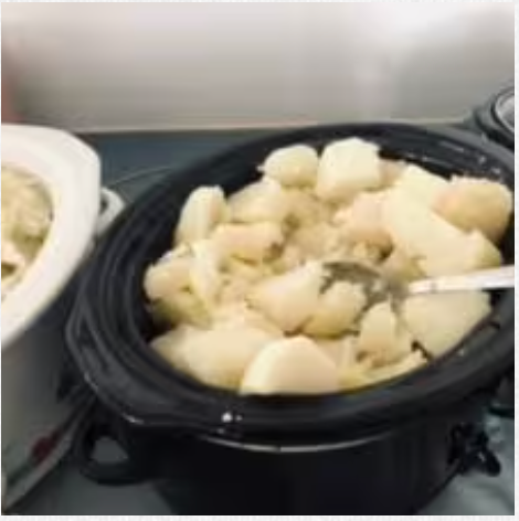 A crock pot filled with potatoes and a spoon in it