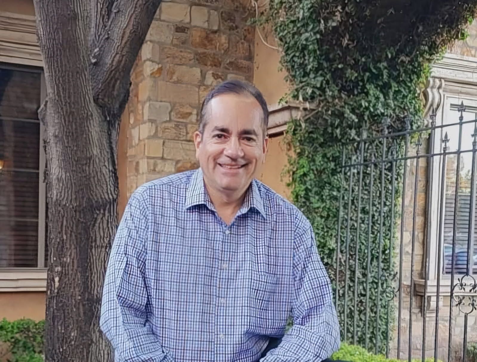 A man in a plaid shirt is sitting in front of a tree.