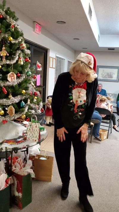 A woman in a santa hat is standing in front of a christmas tree.