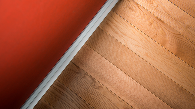 A wooden floor with a red wall in the background