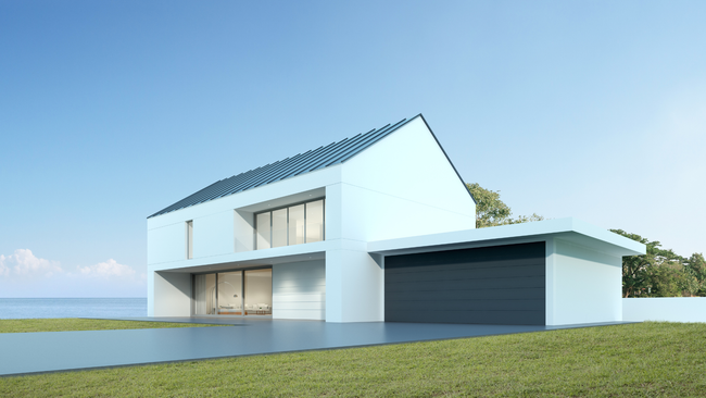 A white house with a black garage door is sitting next to a body of water.