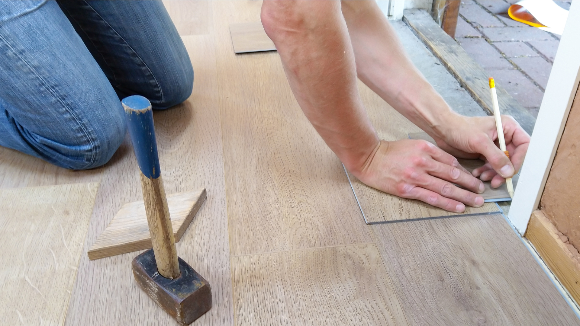 A person is kneeling on the floor measuring a piece of wood.