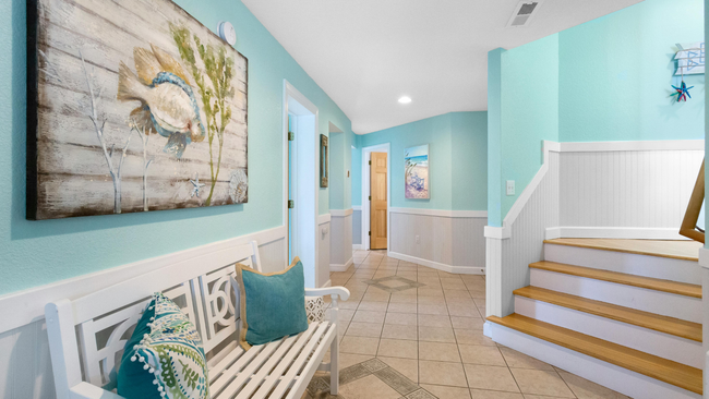 A hallway with a bench , stairs and a painting on the wall.