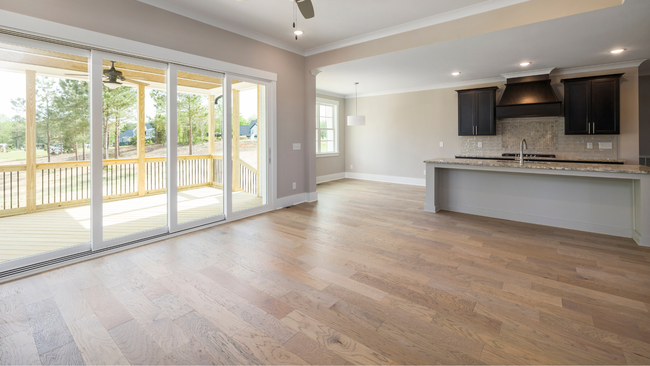 An empty living room with hardwood floors and sliding glass doors leading to a kitchen.