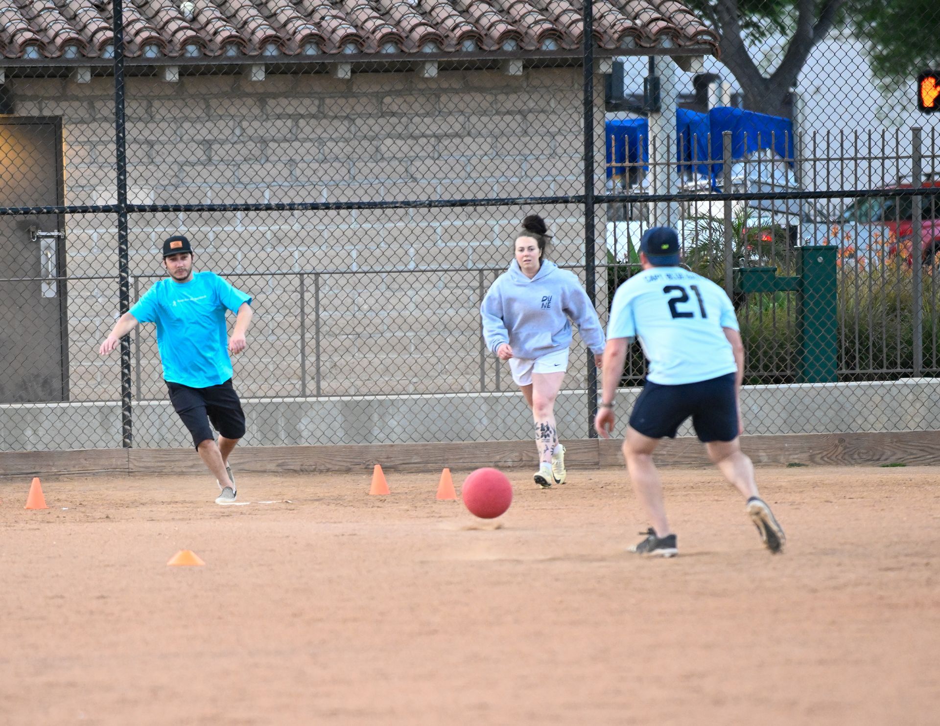 A person wearing a hat and orange shirt, holding a baseball bat on their shoulder on a baseball field.