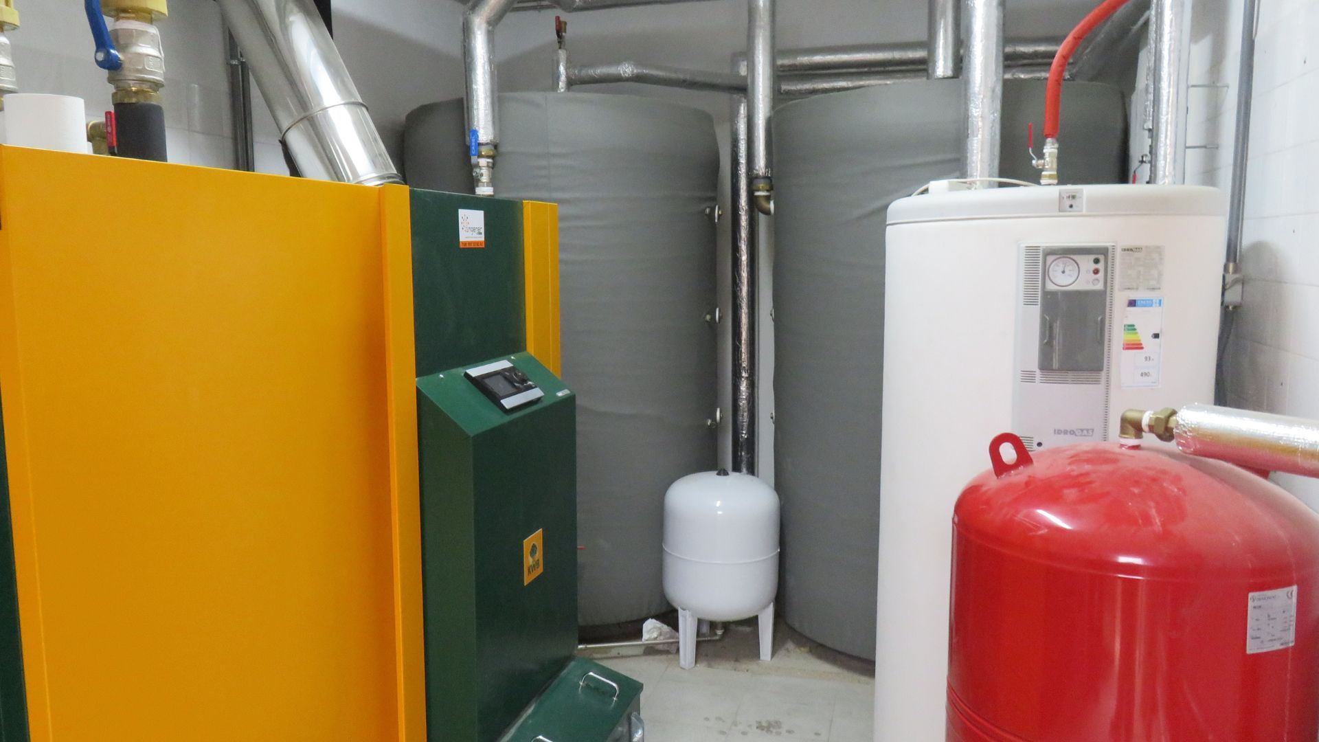 A room with a green and yellow boiler and a red tank.