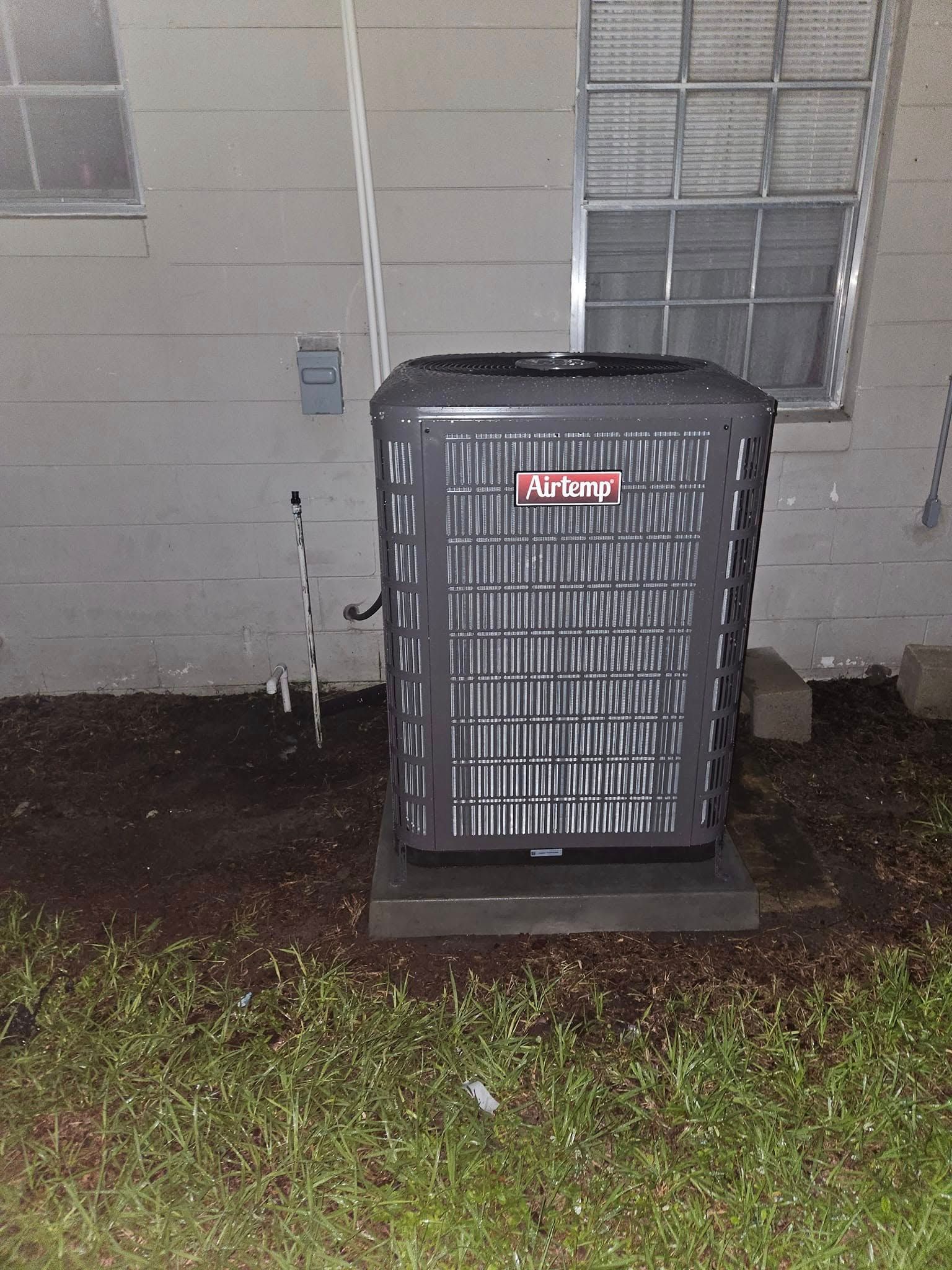 An air conditioner is sitting outside of a house next to a window.