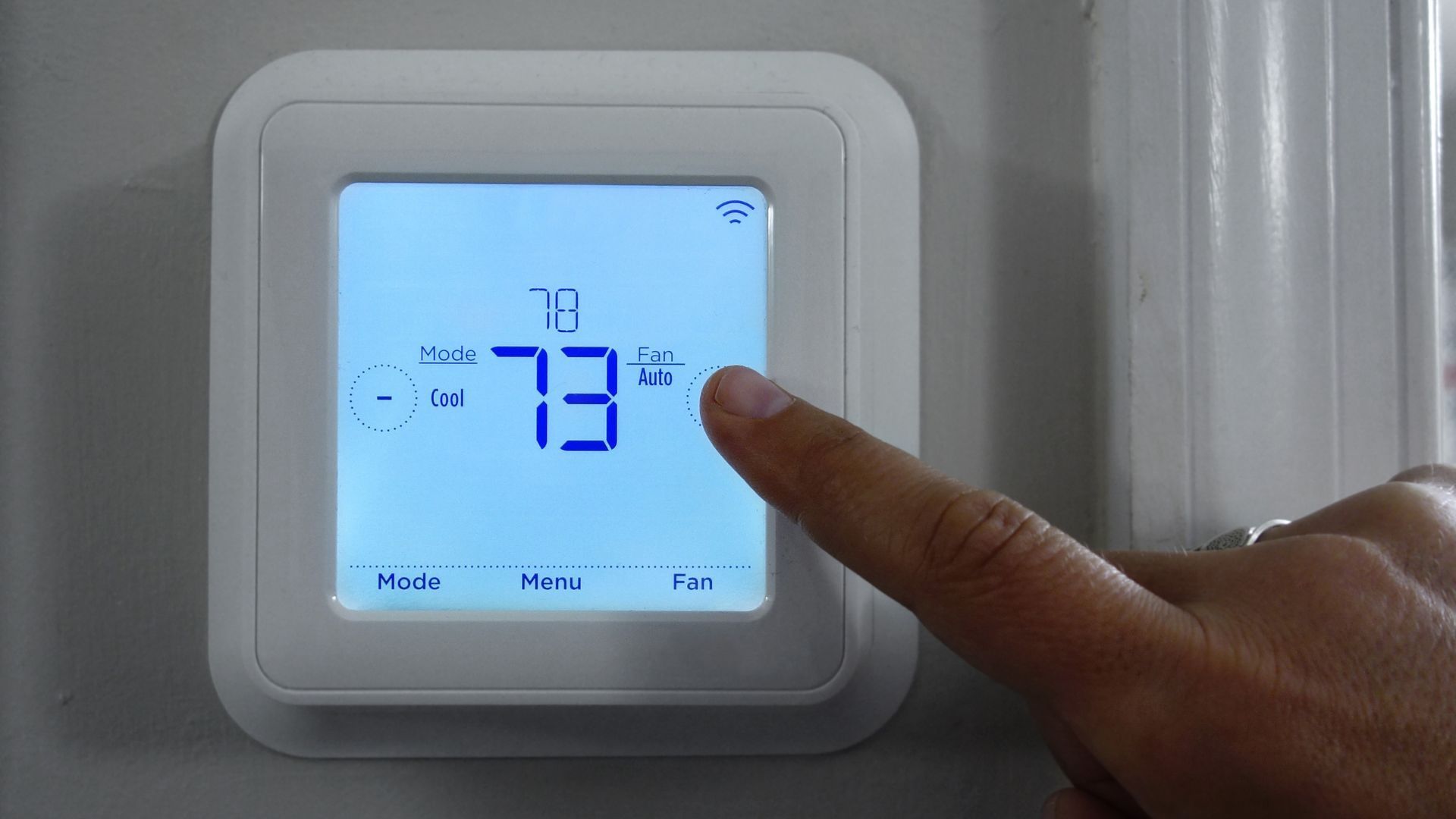 A person is pressing a button on a thermostat.