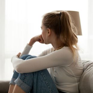 a woman sits on a couch looking out a window